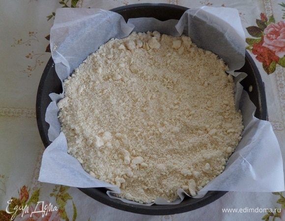 В форму для выпечки, застеленную пергаментом, выкладываем половину охлажденного теста-крошки.