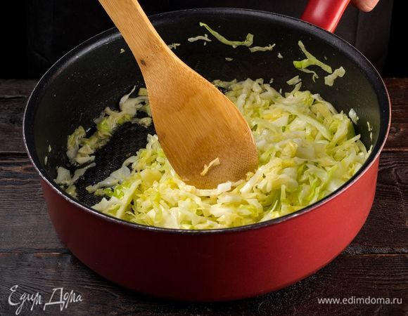 Приготовьте начинку. Для этого капусту нашинкуйте тонкой соломкой и выложите в сковороду. Добавьте немного воды и тушите до выпаривания жидкости. 