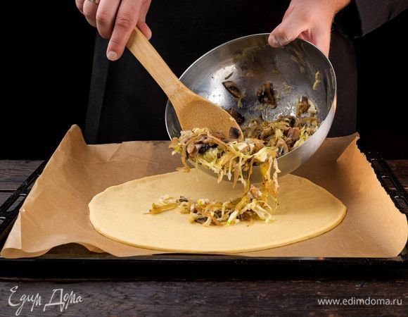 Готовое тесто разделите на 2 части. Одну тонко раскатайте и выложите на застеленный пекарской бумагой противень. Сверху на тесто выложите ровным слоем начинку. 