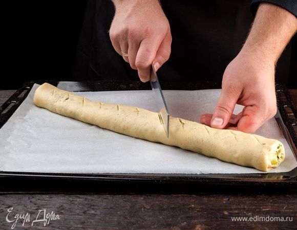 Сверните тесто с начинкой в рулет, выложите на противень швом вниз. Сделайте надрезы. Оставьте тесто на подъем. 