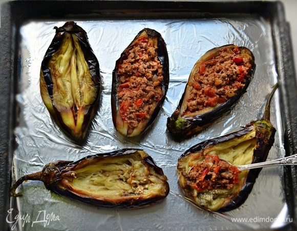 Разложить баклажаны на противень,  выстеланный фольгой и смазанный растительным маслом. Сделать в каждом баклажане продольный разрез и чайной ложкой аккуратно его раскрыть, формируя «лодочку». Заполнить подготовленные «лодочки» начинкой из фарша.