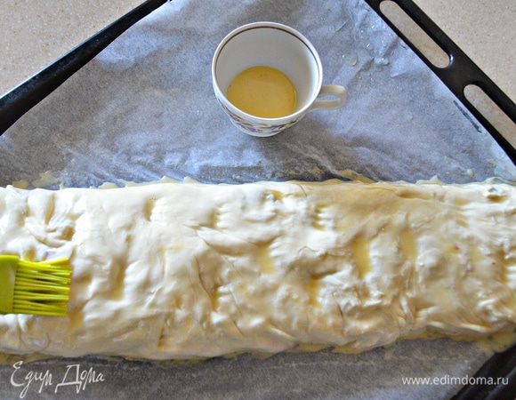 Подвернуть края теста и скатать рулет. Противень выстелить пекарской бумагой, смазать растительным маслом. Аккуратно переложить полученный рулет и смазать его с помощью кисточки желтком.