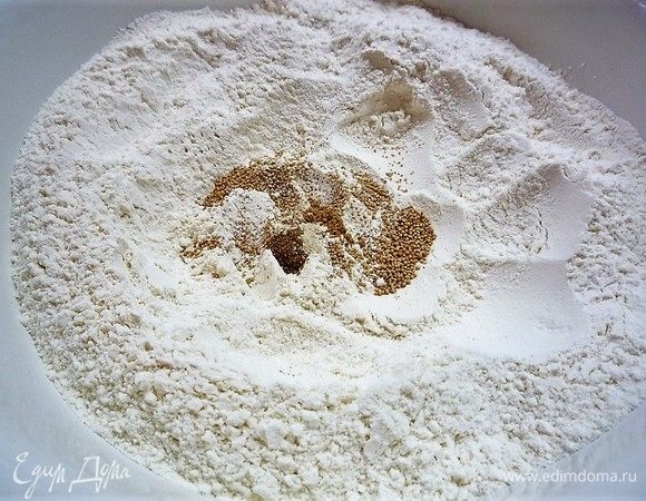 В глубокую чашку высыпаем просеянную муку, добавляем сухие дрожжи и специи (молотые кардамон, имбирь, корицу, гвоздику). Аккуратно размешиваем венчиком. Добавляем 50 г сахара.