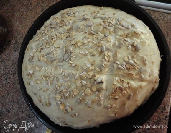 Обомните подошедшее тесто, сформируйте буханку и выложите ее в форму (у меня сковорода диаметром 21 см). Когда булка поднимется, смажьте ее белком и посыпьте смесью овсяных хлопьев и семечек. Сделайте надрезы.