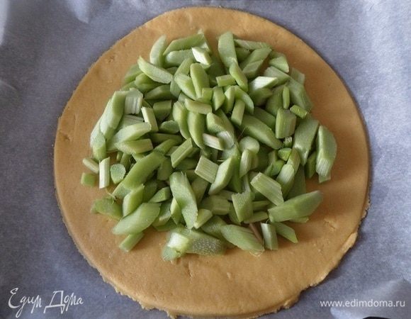 На тесто выкладываем нарезанный ревень, не доходя до краев лепешки 2-3 см.
