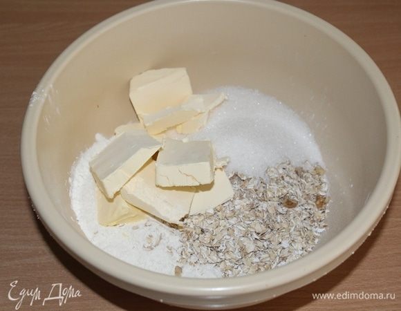 В миске соединить муку, овсяные хлопья, сахар и холодные кусочки сливочного масла. Измельчить все руками в крошку.