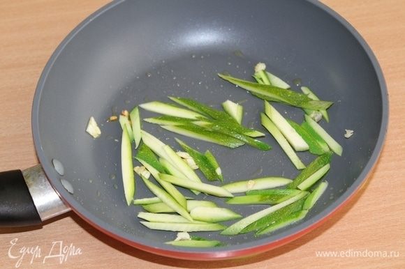 Кожуру с цукини срезать и нарезать соломкой. Обжарить на оливковом масле с долькой чеснока 3-4 минуты.