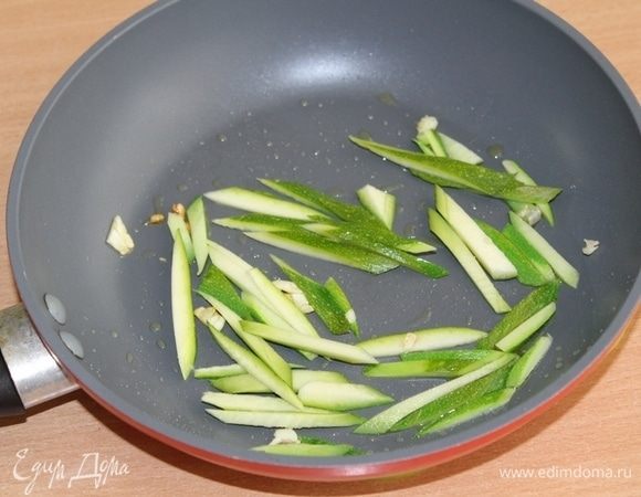 Кожуру с цукини срезать и нарезать соломкой. Обжарить на оливковом масле с долькой чеснока 3-4 минуты.