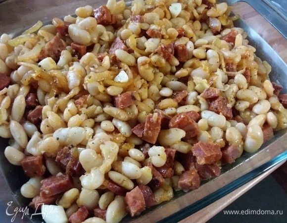 В форму для запекания выложить лук с чоризо, смешать с отварной фасолью, выложить крупно порезанные кусочки чеснока. 