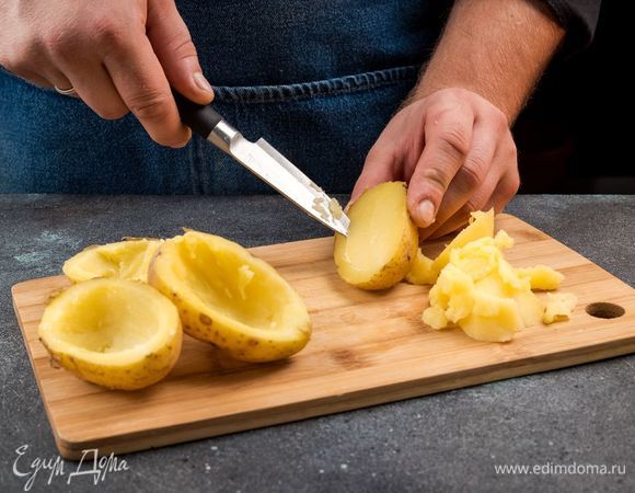 Картофель среднего размера с кожурой хорошо промойте щеткой. Выложите картофель на противень, застеленный пергаментом, сбрызните оливковым маслом и запекайте в разогретой духовке 15 минут. Готовый картофель охладите, разрежьте пополам, выньте часть мякоти, посолите и поперчите. Мякоть картофеля измельчите.