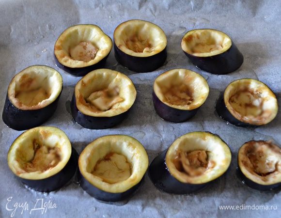 Выложить кружочки баклажанов на противень, застеленный пекарской бумагой и смазанный оливковым маслом. Сбрызнуть баклажаны слегка маслом и запекать в духовке в течение 15 мин. при 180°С.