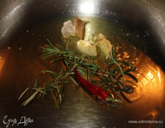 В низкой кастрюле с толстым дном на среднем огне обжарить до золотистой корочки на оливковом масле пеперончино, розмарин, раздавленный плоской частью ножа зубчик чеснока, чтобы масло приняло аромат специй.