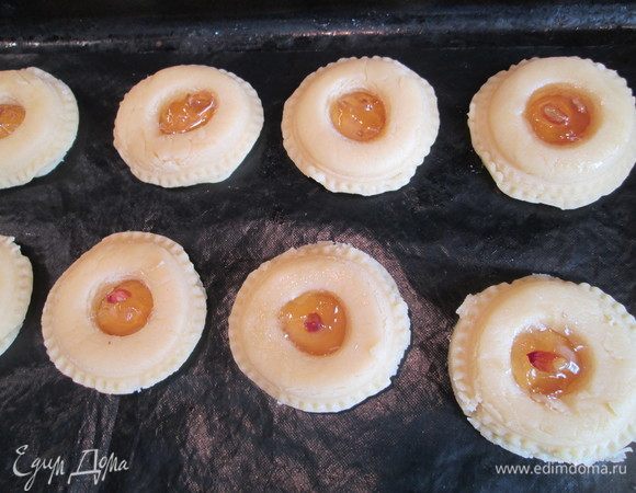 Выкладываем на противень, застеленный силиконовым ковриком. Сверху в каждый кружок добавляем еще джема и стараемся, чтобы в каждый попал кусочек орешка или лимонной цедры. Смазываем яичным желтком, посыпаем кунжутом.