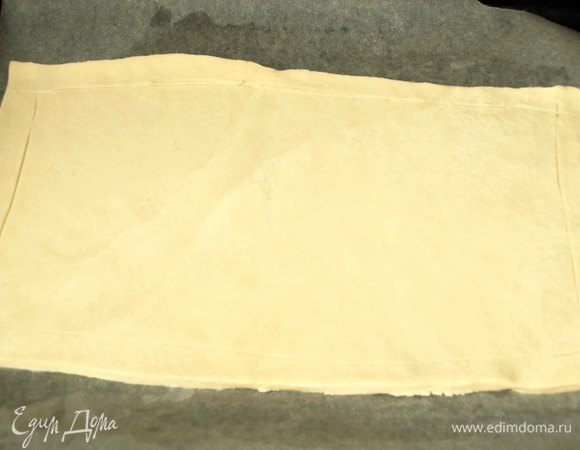 Тесто заранее разморозить. Раскатать пласт и наметить границы, по которым будем выкладывать начинку. Переносим тесто на противень, застеленный пекарской бумагой (смазать растительным маслом) или силиконовый коврик.

