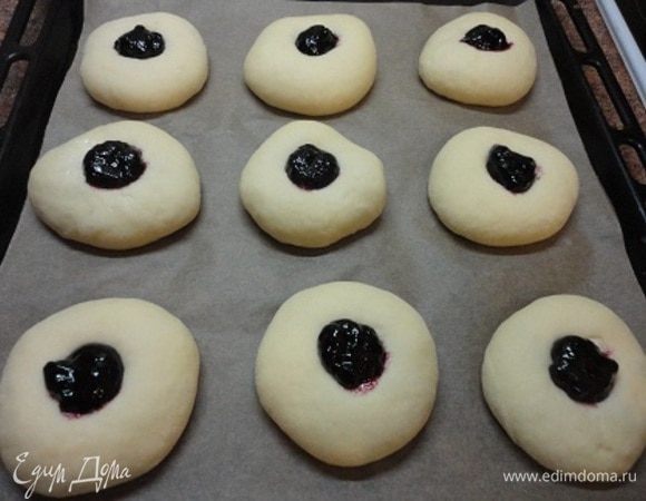Подошедшее тесто разделите на 15 частей примерно по 60-65 г, раскатайте в кружочек, выложите по 1 ч. ложке творога, защипните в центре и выложите на лист швом вниз. Через полчаса нажатием сверху сделайте углубление в булочках с творогом и выложите любимый джем. На фото черничный джем, а на втором листе ватрушки с малиновым джемом. Вот здесь надо было бы смазать белком.