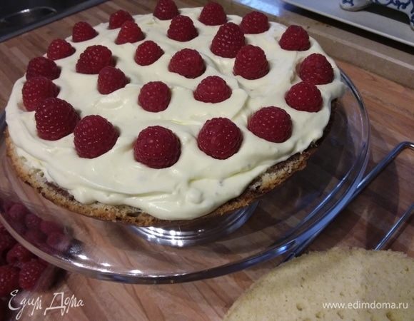 Первый корж выложить на блюдо. Не забудьте нанести немного крема на блюдо, так торт не будет ерзать. На корж выложить часть крема. На крем выложить малину. Крема не жалейте, его достаточно, чтобы нанести толстый слой, в который можно будет наполовину утопить ягоды. 