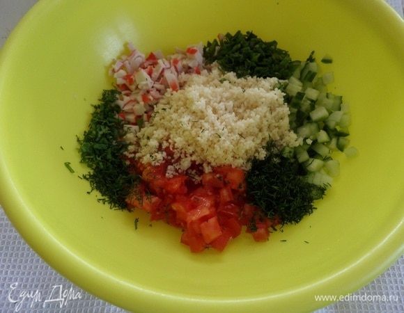 В чашку выкладываем нарезанные овощи, крабовые палочки, зелень, кускус и измельченный зубчик чеснока. Солим по вкусу.