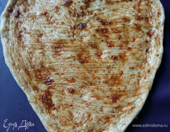 Разделить тесто на 2 части. Одну можно убрать в морозильник. Застелить противень либо бумагой для выпечки, либо ковриком. Взять одну часть теста, руками придать желаемую форму. Мне захотелось в форме сердечка. Нанести с помощью силиконовой кисточки аджику на всю поверхность. Можно заменить кетчупом, кому как нравится.