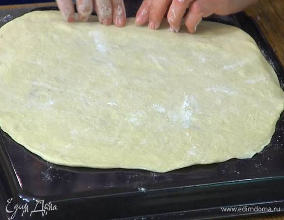Обратную сторону противня смазать оливковым маслом и равномерно распределить раскатанное тесто.