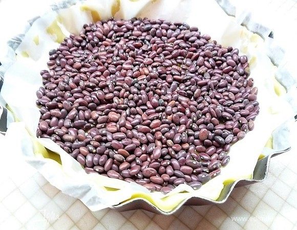 Поверх теста укладываем бумагу для выпечки и высыпаем на нее фасоль. Выпекаем в заранее разогретой духовке при температуре 190°С в течении 15 минут, затем бумагу с фасолью убираем и выпекаем еще 10 минут.