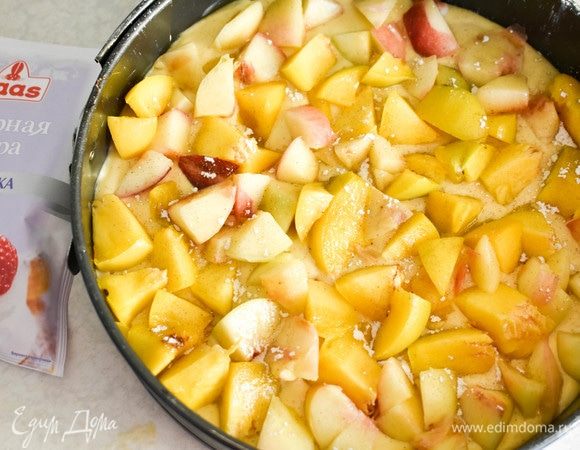 В разъемную форму выкладываем тесто, выравниваем сверху персики, нарезанные кубиками. Слегка посыпаем их сахарной пудрой.