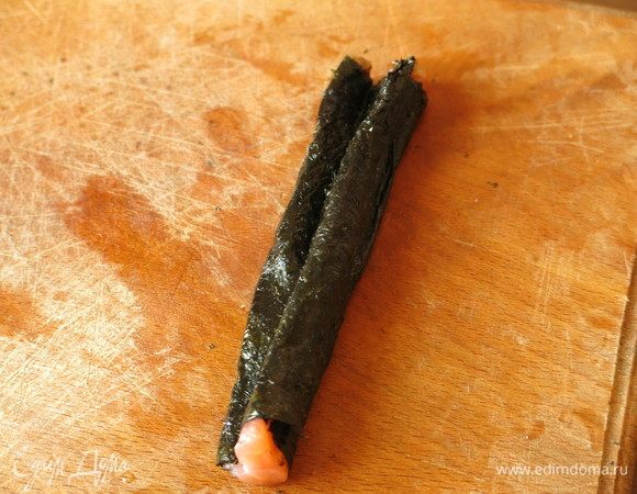 Завершаем обертку, срезаем лишний лист нори, получается кусочек семги с двумя зубчиками в нори — это хвост рыбы.