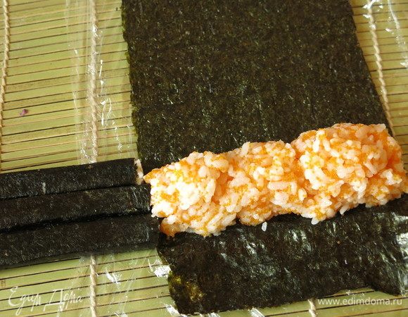 На лист суши — ширина равна длине палочек — отступив от края 2–3 см выкладываем горкой рис цветной, ширина основания должна равняться трем палочкам. Легко положить палочки и по их размеру формировать рис.