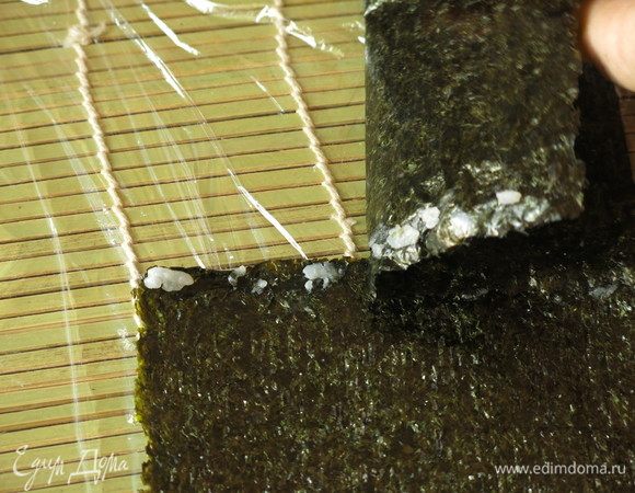 Сборка кадзари — еще разрезаем 2 нори по длине палочек. Две полоски нори соединяем, но уже не водой, а рисинками, для прочности — раскладываем рисинки по краю, кладем лист сверху и прижимаем.