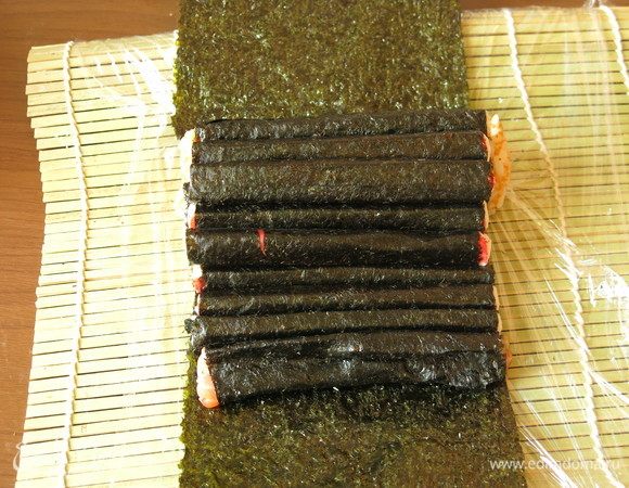 Выкладываем поперек листа нори рулон с оранжевым рисом, горкой рулоны с палочками — 3 шт., 3 шт., 2 шт., 1 шт., 1 шт., рулон с красной рыбой.