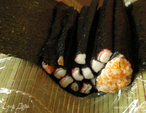 Вид сбоку. Держим закругленный коврик снизу, как раз заготовка помещается в ладонь. Палочки должны лечь срезом к роллу с оранжевым рисом — это чешуя, фактурность палочек, их слоистость создает дополнительный рисунок.