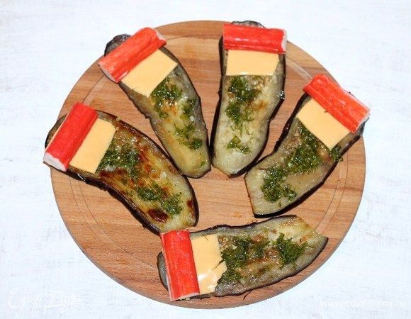 Раскладываем укропный соус на пластины баклажана. Кладем по 1 кусочку сыра. Сверху кладем крабовые палочки.