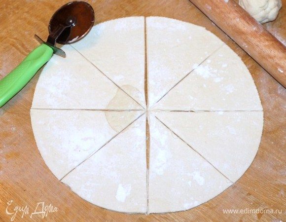 Приготовим тесто. Достаем размороженное тесто из упаковки. Присыпаем столешницу мукой и раскатываем тесто. Вырезаем круг диаметром 28 см. Разрезаем круг на 8 частей.