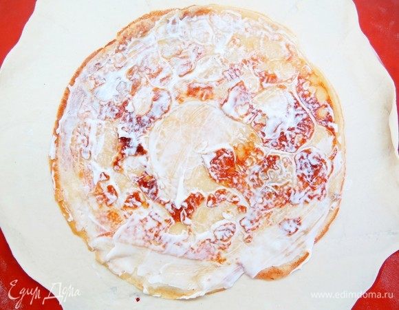 На раскатанное тесто выкладываем в центр первый тонкий блинчик. Смазываем блинчик сметанно-горчичной заправкой.