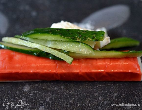 Лист рисовой бумаги замочить на 5 минут в теплой воде. Затем выложить его на тарелку, на него — крабовую палочку, чайную ложку творожного сыра и несколько соломок огурца.