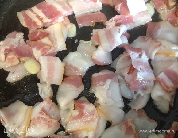 Чеснок нарезать тонкими ломтиками и обжарить на оливковом масле до золотистого цвета. Добавить нарезанный небольшими кусочками бекон и готовить 4 мин.