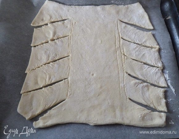 Переносим тесто на противень, застеленный пергаментом. Визуально делим прямоугольник теста на 3 равные части. Обе боковые части нарезаем на ленты.