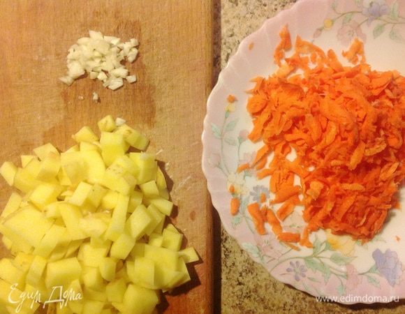 Нарезать картофель кубиками. Мелко порубить чеснок. Морковь натереть на крупной терке.