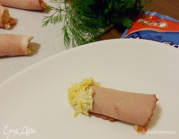 Затем обмакнуть один край рулетика сначала в оставшийся майонез, а затем — в тертое яйцо.