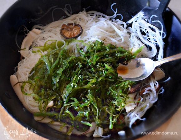 Обжарьте в течение 2 мин. шиитаке, добавьте кальмары, перемешайте и обжаривайте еще 1,5 мин., интенсивно перемешивая. Затем добавьте готовую рисовую лапшу и водоросли чука, а также немного соевого соуса, хорошо все перемешайте и выключите огонь.