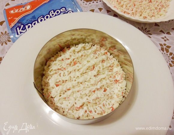 Я буду подавать салат порционно, поэтому воспользуюсь формовочным кольцом. Каждый слой перед нанесением майонеза необходимо совсем немного утрамбовать. Выложить половину крабового мяса на дно сервировочной тарелки и нанести сеточку из майонеза.