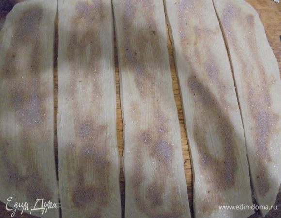 Подошедшее тесто раскатать в прямоугольный пласт размером 30 на 50 см. Смазать тесто растопленным сливочным маслом, посыпать смесью сахара и корицы. Нарезать поперек на 6 полосок.