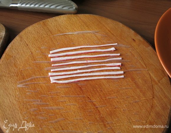 Выкладываем аккуратно мокрый лист на досточку. Отступив от края 2-3 см, выкладываем зеброй полоски краба.