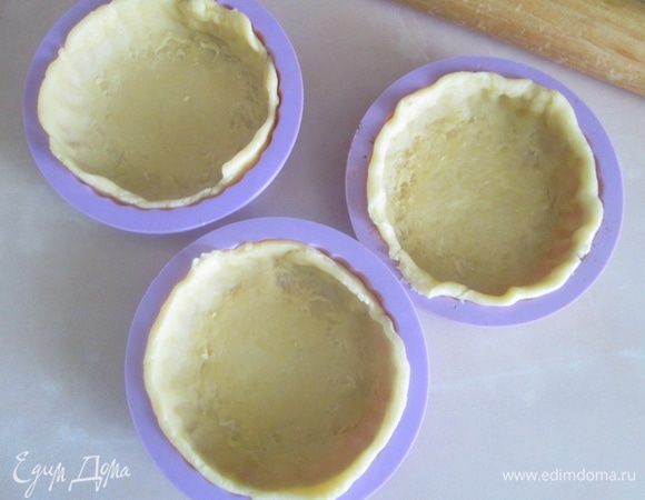 Холодное тесто разделить на равные кусочки, раскатать в тонкий пласт и выложить в формочки. В дно и бока формы аккуратно вдавить тесто, убрать излишки.