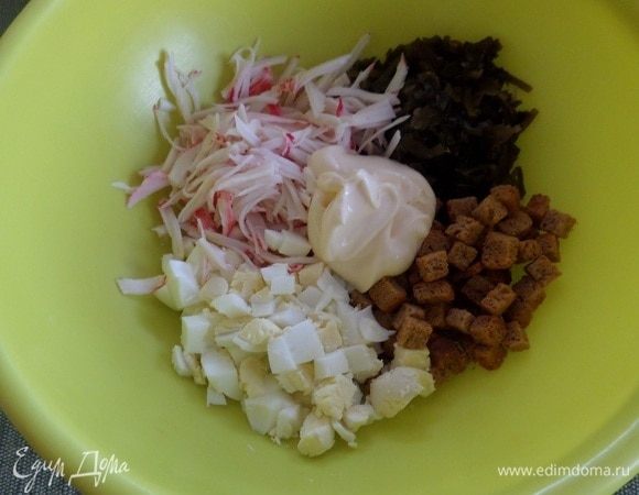 Выкладываем в чашку сухарики, морскую капусту, нарезанное яйцо и крабовые палочки. Добавляем майонез. 