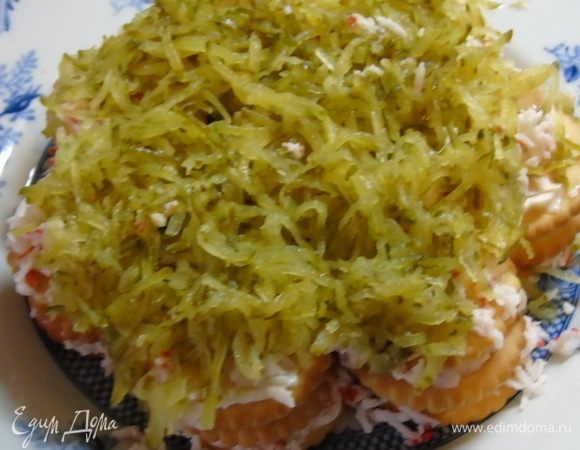 Опять слой крекера, смазать майонезом и выкладываем оставшиеся крабовые палочки, снова слой крекера, и поверх тертый огурец.