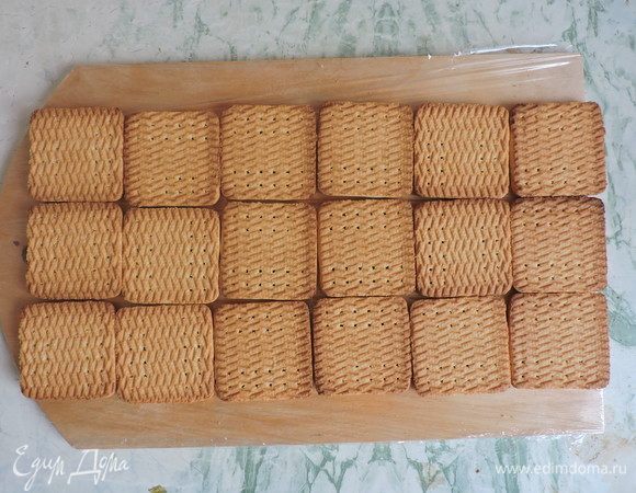 Выложим нижний слой нашего торта, для этого пищевой пленкой застелем доску и выложим печенье. Всего нам понадобится 36 штук печенья (это примерно 400 г). Будет два слоя, каждый по 18 штук, печенье быстро макаем в теплое молоко и укладываем в прямоугольник как на картинке (3х6).