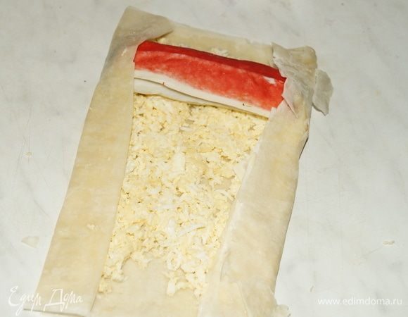 На один край теста выложить крабовую палочку со шпинатом, загнуть края и свернуть рулетом.