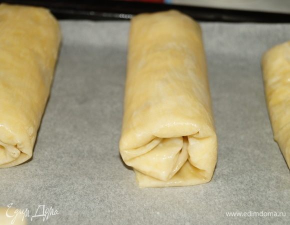На противень, застеленный бумагой для выпечки выложить подготовленные рулетики и смазать их сливочным маслом. Выпекать в духовке при 180°C около 20 минут или до румяной корочки.