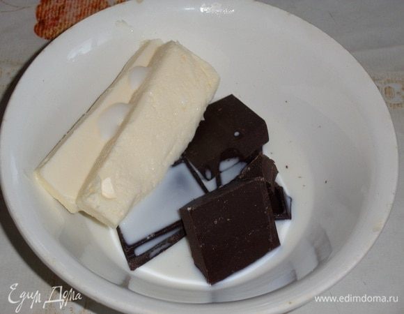 В чашку выкладываем шоколад и сливочное масло. Добавляем молоко. Накрываем чашку.  Помещаем чашку в микроволновую печь при максимальной мощности на 30 секунд, затем добавляем еще 1-2 раза по 10 секунд.