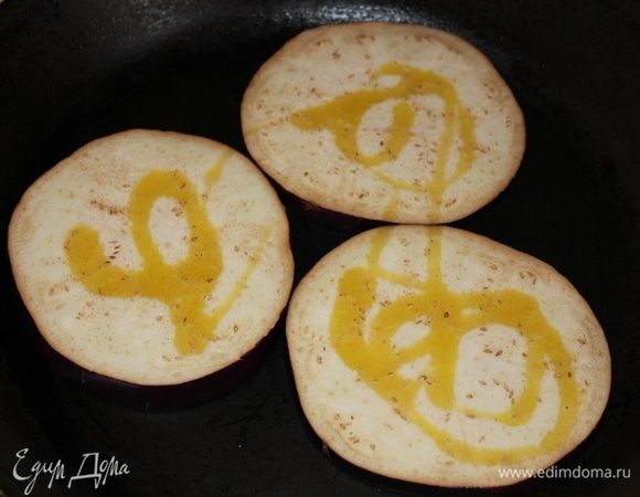 Отрезать от крупного баклажана 3 ломтика-круга толщиной около 1 см., выложить на раскаленную сковороду, смазанную небольшим количеством оливкового масла. Сразу сбрызнуть оливковым маслом ломтики и сверху. 